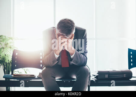 Imprenditore disperato in sala d'attesa con testa in mani, egli è in attesa di un colloquio di lavoro; la disoccupazione e il fallimento aziendale concept Foto Stock