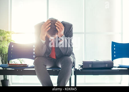 Imprenditore disperato in sala d'attesa con testa in mani, egli è in attesa di un colloquio di lavoro; la disoccupazione e il fallimento aziendale concept Foto Stock