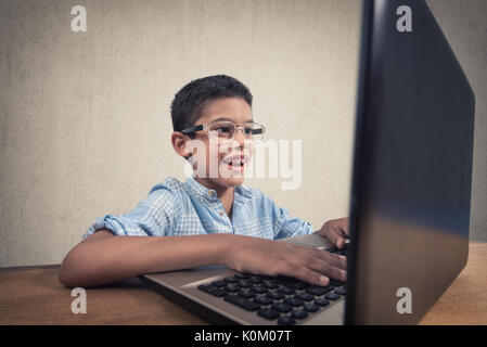 Felice ragazzo seduto alla sua scrivania con computer portatile Foto Stock