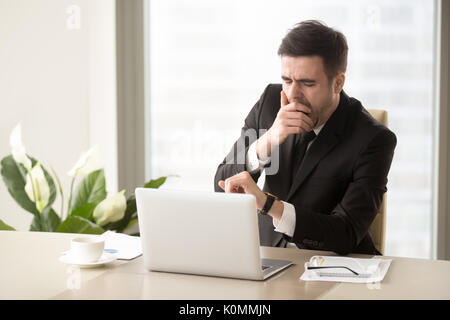 Stanco imprenditore annoiati sbadigli al posto di lavoro, tempo di controllo su w Foto Stock