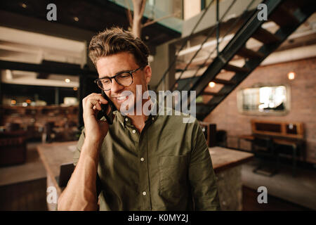 Colpo di felice giovane uomo facendo una telefonata. Executive sorridente parlando al telefono cellulare in ufficio. Foto Stock