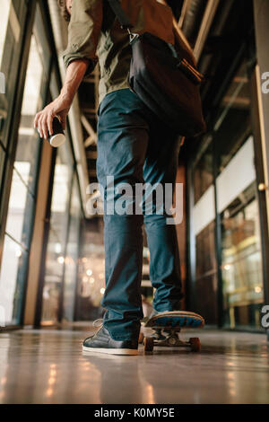 Vista posteriore del colpo di uomo con lo skateboard in ufficio. Giovane imprenditore pattinaggio attraverso office corridoio. Foto Stock