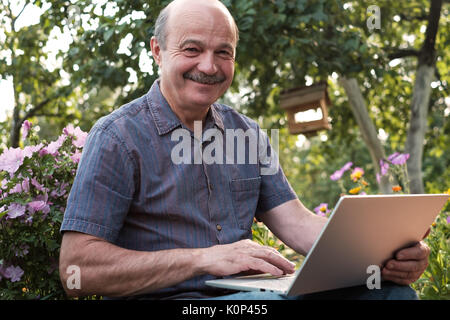Uomo maturo seduti in giardino in campagna con il notebook e il relax Foto Stock
