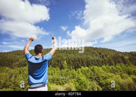 Vista posteriore dell'uomo con le braccia sollevate in piedi nella foresta contro mountain Foto Stock