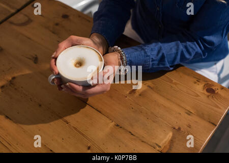 Elevato angolo di visione della donna azienda tazza da caffè a tavola in cafe Foto Stock