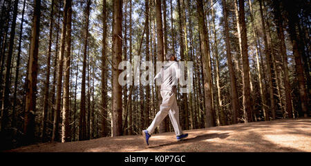 Vista laterale del giovane uomo che corre sulla strada da alberi in foresta Foto Stock
