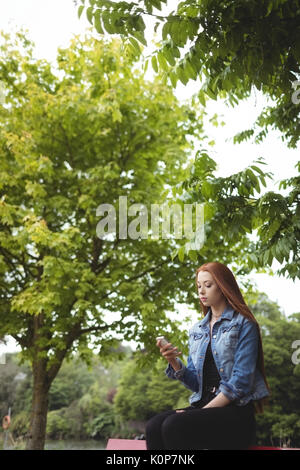 Giovane donna utilizza lo smartphone mentre è seduto su un banco di lavoro in posizione di parcheggio Foto Stock