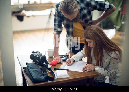Elevato angolo di visione Uomo cerca Donna a scrivere sul libro a tavola in studio Foto Stock