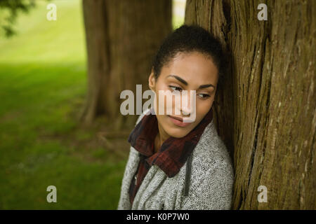 Close-up di pensosa donna appoggiata sul tronco di albero Foto Stock
