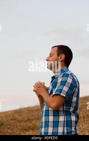 Uomo che prega fuori da solo su un lato di una collina. Foto Stock