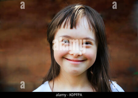 Carino sorridente la sindrome di down ragazza sullo sfondo marrone Foto Stock