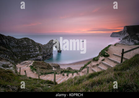 Un drammatico tramonto magenta su una serata estati a Durdle porta sul Jurassic Coast in Dorset, un sito del Patrimonio Mondiale prese con una lunga esposizione Foto Stock