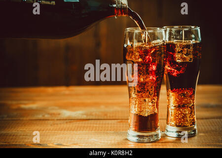 Versando bella bevanda fredda di cola con cubetti di ghiaccio con una caldaia cannucce in bicchieri su sfondo di legno con spazio libero Foto Stock