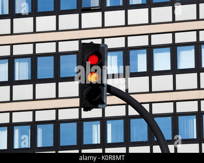 Il traffico con luce rossa e le luci color ambra brillante sullo sfondo di bianco moderno ed alto edificio di uffici con il blu del cielo si riflette in Windows Foto Stock