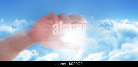 Mano di uomo fingendo di tenere un oggetto invisibile contro le nubi contro il cielo blu Foto Stock