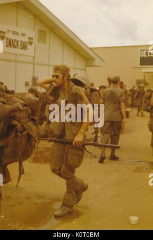 Un folto gruppo di soldati in uniforme con piena lotta ingranaggio, attende il trasporto al di fuori degli edifici a 8 porta antenna, Bien Hoa Air Base, Vietnam, 1964. Foto Stock