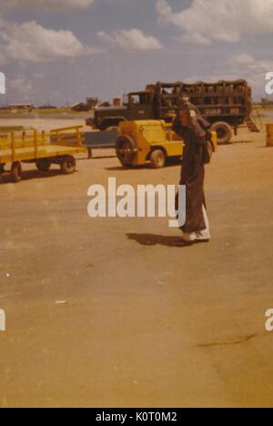 Il vietnamita uomo a camminare su di un aeroporto Aeroporto e attrezzature militari visto in background, l'unità Phu Bai Base di combattimento, Vietnam, 1964. Foto Stock