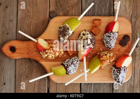 Caramello e cioccolato immerso fette di mela su una scheda a pale con rustico sfondo di legno Foto Stock