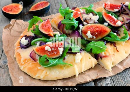 In autunno il pane piatto pizza con fichi, rucola e formaggio di capra, close up su uno sfondo di legno Foto Stock