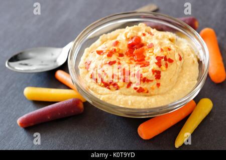 Spicy hummus dip e baby rainbow carote close up su un sfondo di ardesia Foto Stock