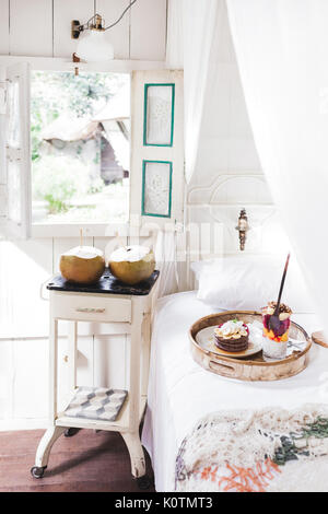 Fresh gustosa colazione a letto su vassoio in legno Yogurt con frutta e chia, frittelle di miele, due toast con avocado e uova in camicia e due giovani cocon Foto Stock