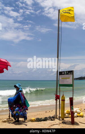 Kamala Beach, Phuket, Tailandia. 24 Ago, 2017. Un venditore passeggiate passato un giallo "bagnino di turno" bandiera. Molti turisti ignora lifeguard avvertenze e senza zone di nuoto risultante in numerosi decessi per anno a Phuket. Credito: Kevin hellon/Alamy Live News Foto Stock