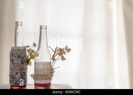 Decorativo di bottiglie di vetro su un morbido sfondo retroilluminato, con piccoli fiori sul lato Foto Stock