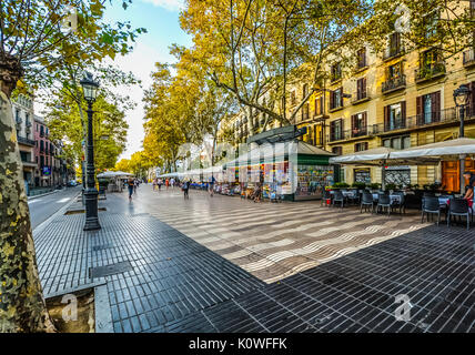 Mattina sulla Rambla di Barcellona Spagna prima i turisti arrivano come un cafè diventa pronto per il business e una donna acquista souvenir da un cavalletto Foto Stock