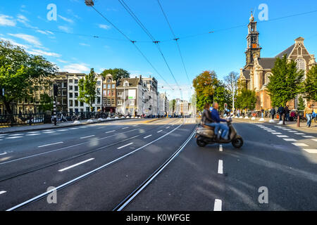 Un giovane su una vespa o scooter attraversare un incrocio attraverso un vuoto street in Amsterdam Foto Stock