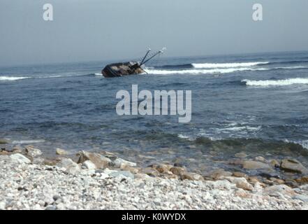La pesca in barca sommersa dalle onde e affondamento fuori dalla riva di una spiaggia rocciosa, arenamento con il suo scafo in corrispondenza di un angolo e tenuto sull'acqua, Gloucester, Massachusetts, 1952. Credito Foto Collezione Smith/Gado/Getty Images. Foto Stock
