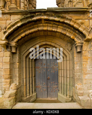 Porta ad arco ornato di cerniere è circondato da una serie di motivi decorativi archi di pietra a storico priorato di Tynemouth rovine, Inghilterra Foto Stock