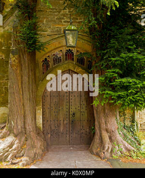 Insolito porta ad arco incorniciato da tronchi di vecchi di 200 anni yew alberi presso medieval St. Edward's chiesa a Stow-su-il-wold, Inghilterra Foto Stock