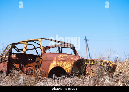 Abbandonato e arrugginito relitto di un giallo sovietica vintage vettura russa nel mezzo di fieno secco con scenic ghiaccio montagne superiore nel sud dell'Armenia Foto Stock