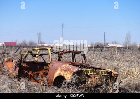 Abbandonato e arrugginito relitto di un giallo sovietica vintage vettura russa nel mezzo di fieno secco con scenic ghiaccio montagne superiore nel sud dell'Armenia Foto Stock