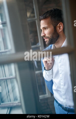 Uomo bello in studio guardando attraverso la finestra aperta Foto Stock