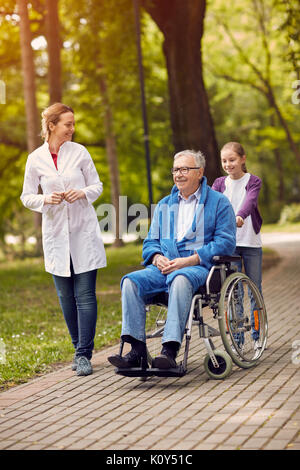 Ritratto di uomo anziano sulla sedia a rotelle con il caregiver infermiere e nipote outdoor Foto Stock