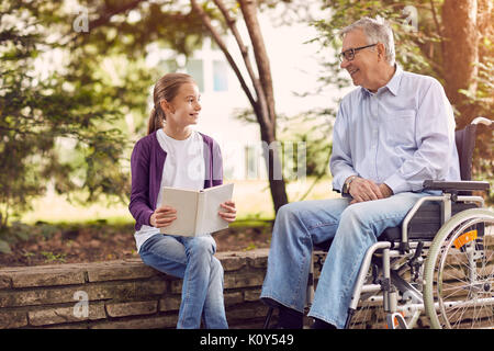 Nonno disabili nel parco di trascorrere del tempo insieme con il suo nipote libro lettura outdoor Foto Stock