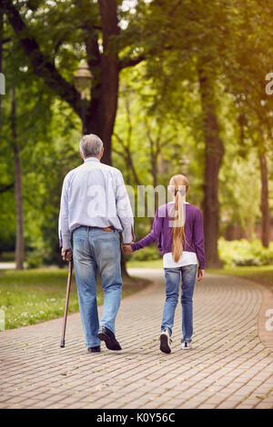 Ragazza e il nonno disabili tenendo le mani sulla passeggiata nel parco Foto Stock