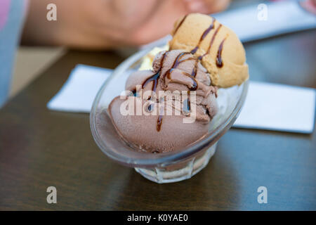 Vicino la vista dettagliata di gustoso cioccolato e caramello gelato alla crema con salsa al cioccolato servito in tazza di vetro. Foto Stock