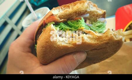 Tenendo un hamburger con morso mancante in mano. Fast food mangiare malsano. Foto Stock