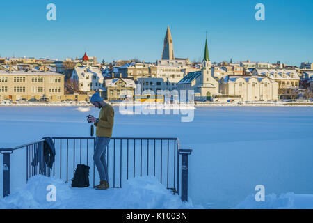 Uomo che guarda la sua macchina fotografica al laghetto congelato a Reykjavik, Islanda Foto Stock
