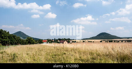 Campagna con prato, campo Brezno village, alberi, colline isolate di Ceske stredohori mountain range e cielo blu con nuvole in Repubblica Ceca Foto Stock