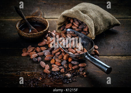Cacao in polvere in un recipiente e le fave di cacao su sfondo di legno Foto Stock