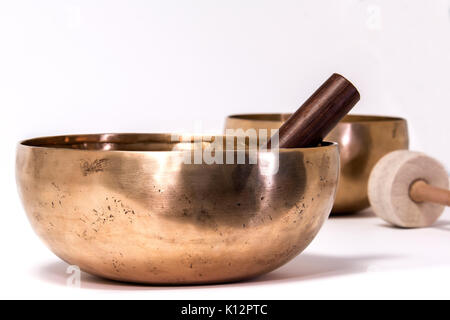 Due di bronzo in lega di rame SINGING BOWLS con uno di colpire e uno sfregamento mazzuoli su sfondo bianco. Foto Stock