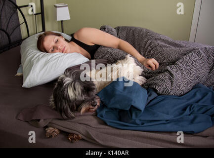 Giovane donna con il rosso marrone capelli addormentato nel suo letto con i suoi due cani raggomitolati accanto Foto Stock