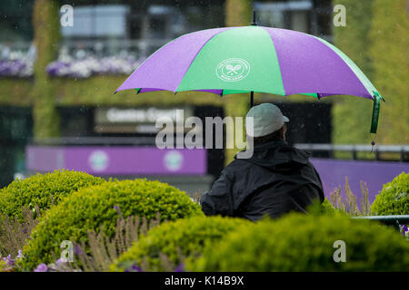 Una ventola con un ombrello di Wimbledon nella pioggia a campionati di Wimbledon 2017 Foto Stock