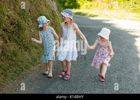 Tre giovani ragazze francesi, sorelle, camminare mano nella mano per mano lungo un paese francese strada in estate. Essi sono di età compresa tra i 3, 5 e 7 anni.(89) Foto Stock