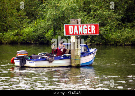 Uomo con attività di pesca in una piccola motonave attraccata nel mezzo del fiume Tamigi legato ad un palo di legno dicendo pericolo Foto Stock