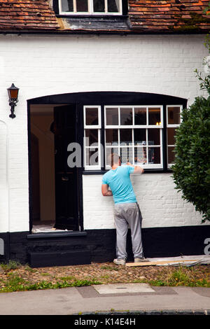 L'uomo pittura le finestre del vecchio ufficio postale in high street Dorchester on Thames Oxfordshire un vecchio nero e bianco edificio Foto Stock