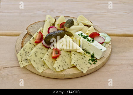 Vari formaggi diversi disposti su un piatto di legno con pomodori, sottaceti e il coltello. Foto Stock